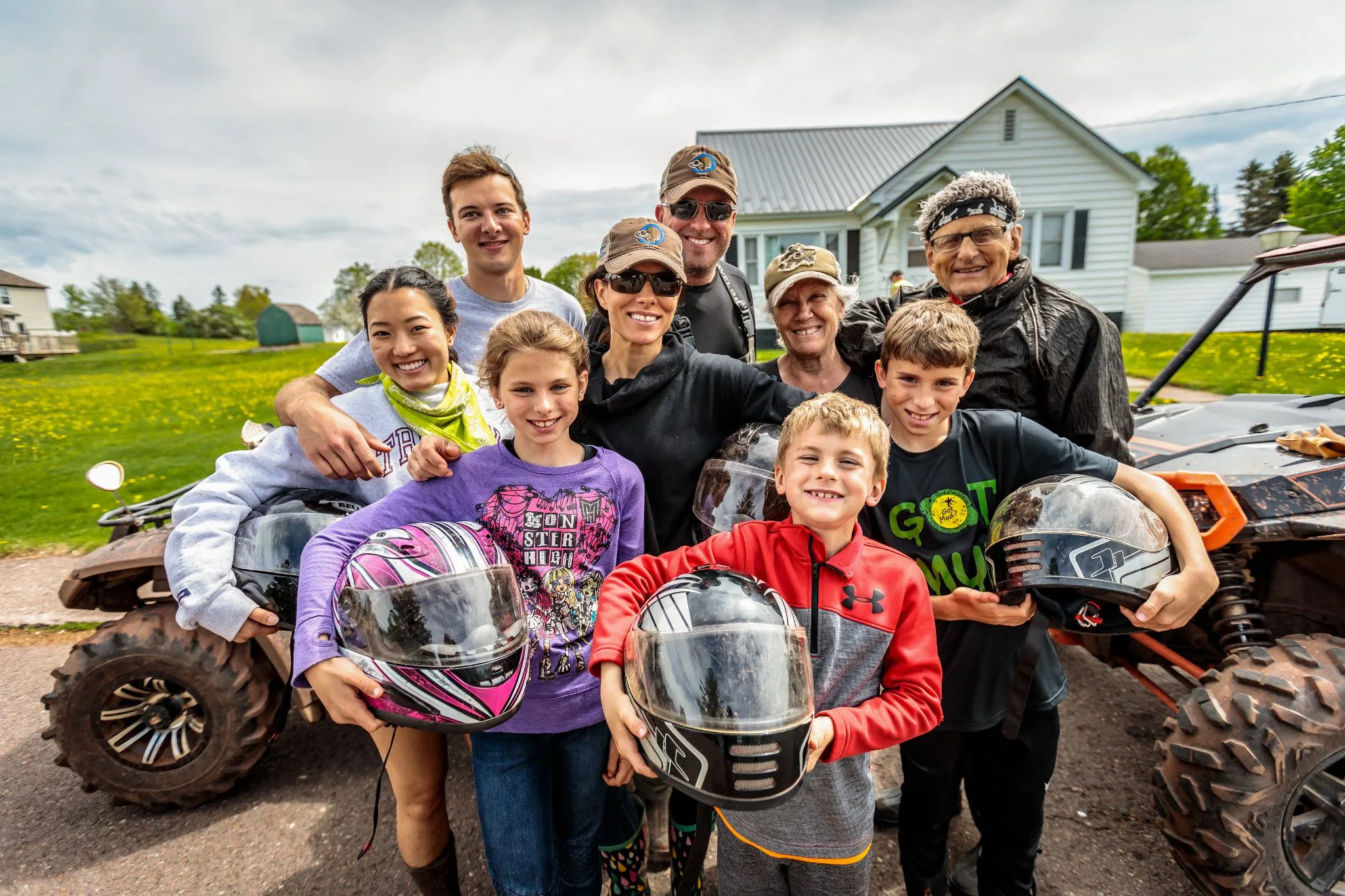 A group of adults and children pose outside of ATVs with helmets A group of adults and children pose outside of ATVs with helmets